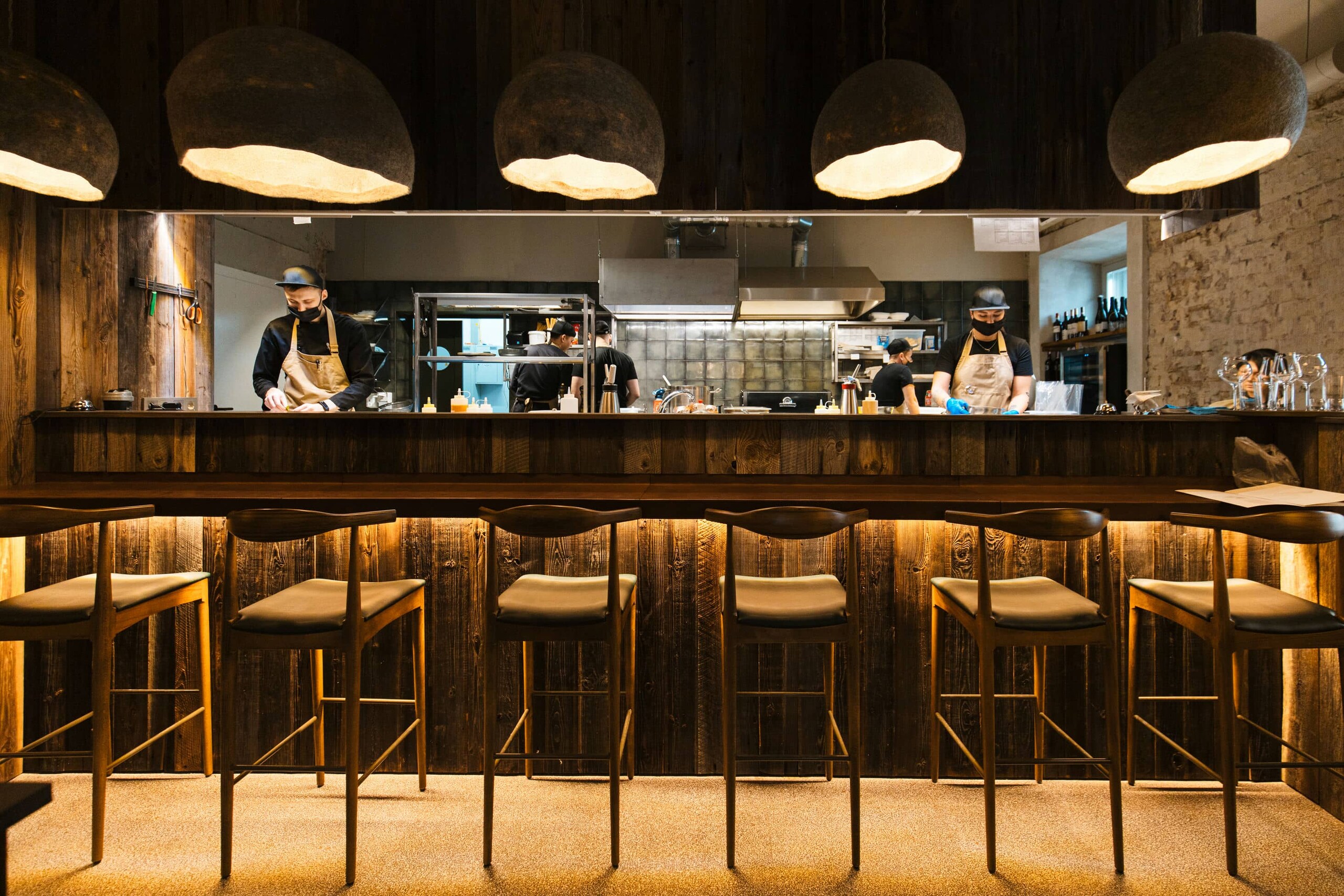 Chefs at work in open kitchen at a restaurant, with a row of stools in front of the counter